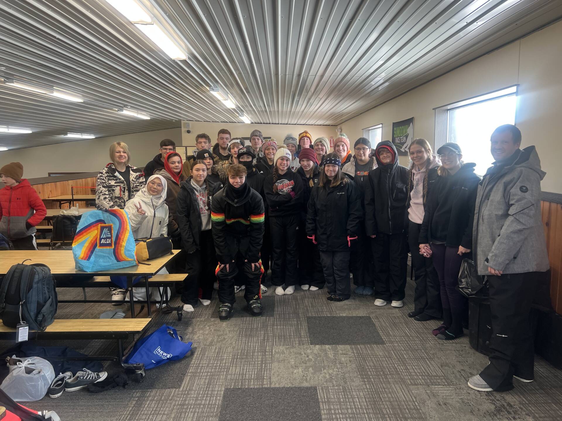 A group of bundled-up students and chaperones pose together inside a ski lodge during a winter field trip.