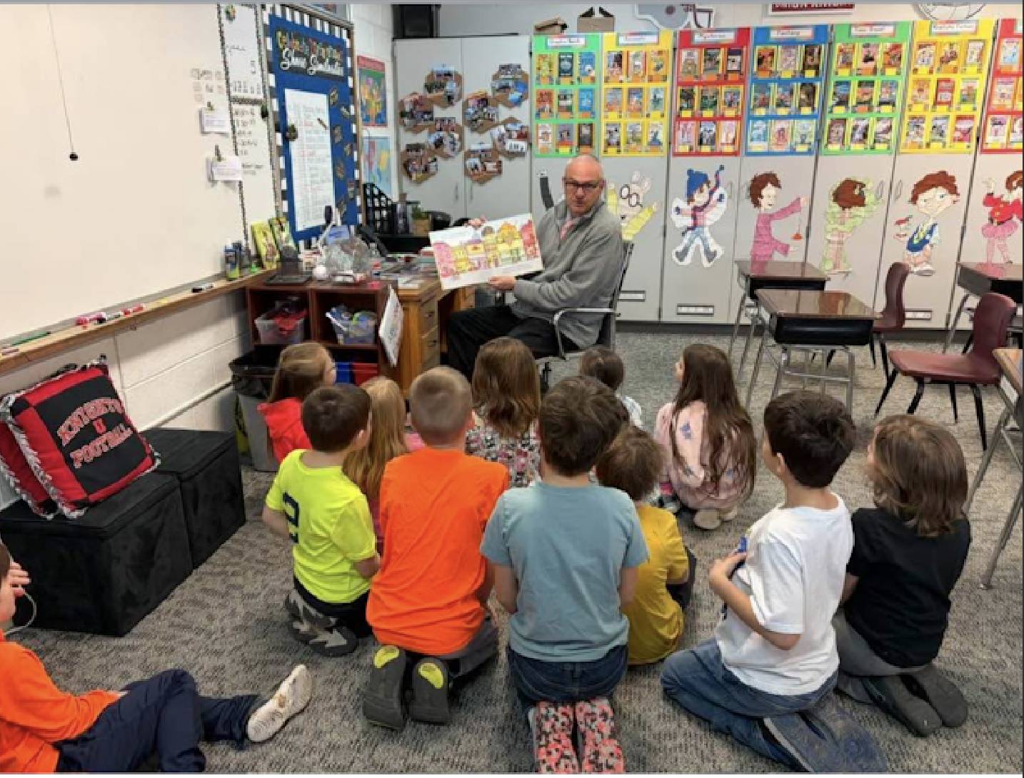 A teacher reads a picture book to students seated on the floor during story time in an elementary classroom.