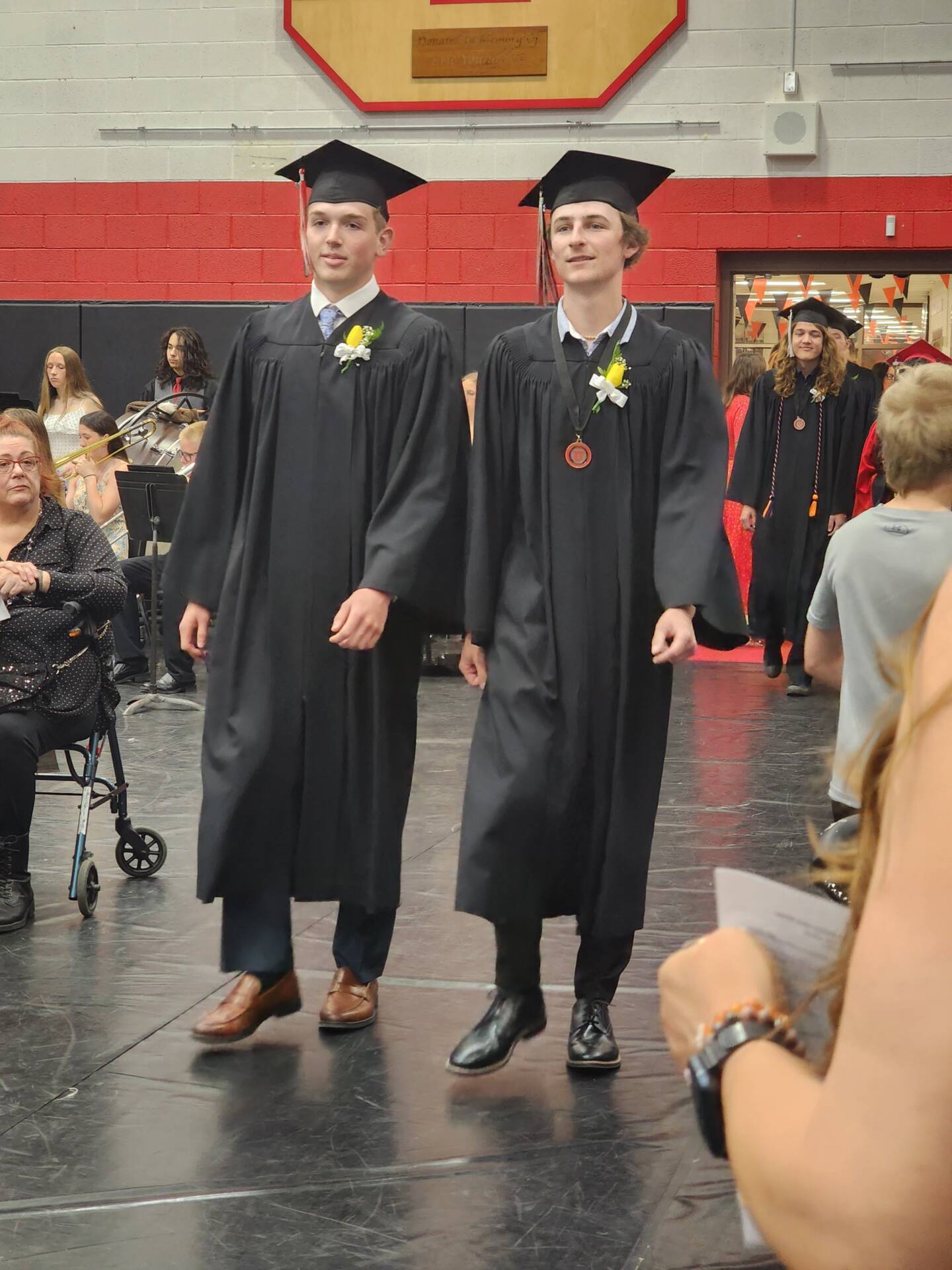 Two graduates in black caps and gowns walk into the gymnasium during the graduation ceremony.