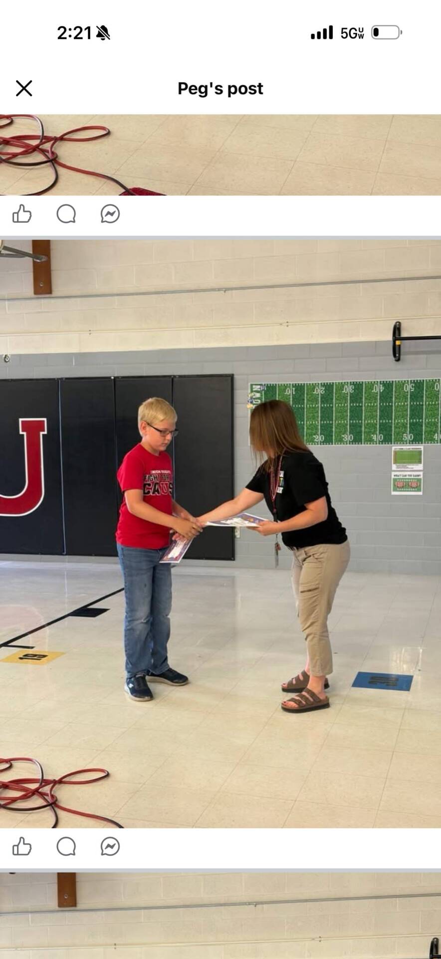 Staff member presents a certificate to a student during an elementary school promotion ceremony in the school gym.