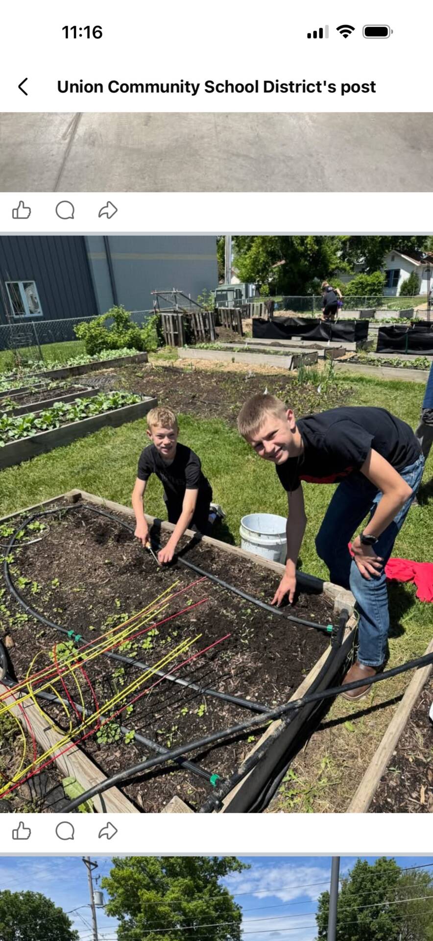 Two students work in a community garden, tending a raised planting bed on a sunny day.