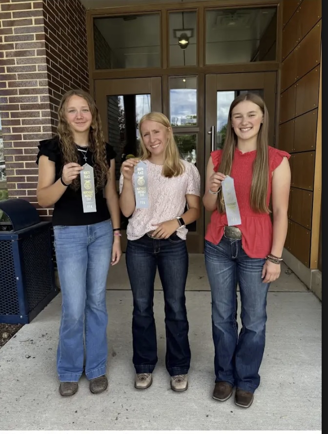 Three FFA students display award ribbons while posing outside a building entrance.