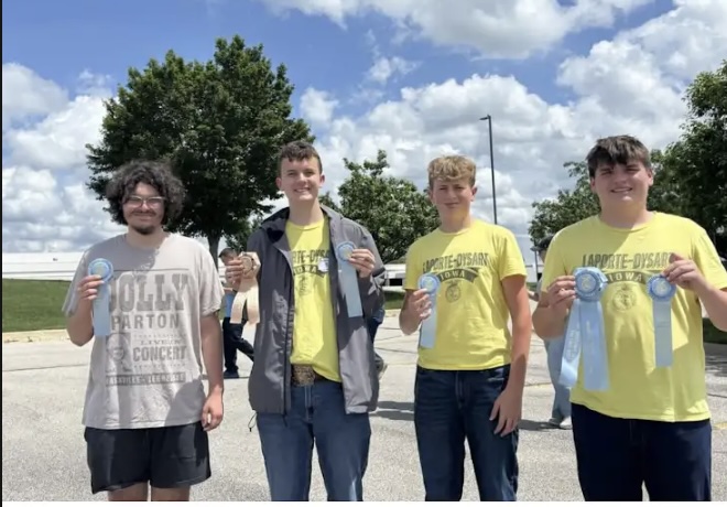 Students display award ribbons earned at a competition while posing outdoors on a sunny day.