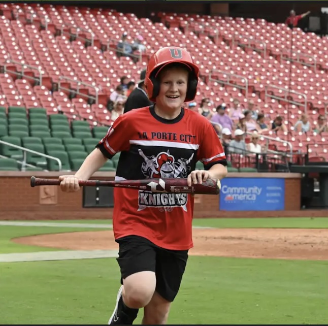 Young Porte City Knights player runs across the field holding a bat at Busch Stadium.