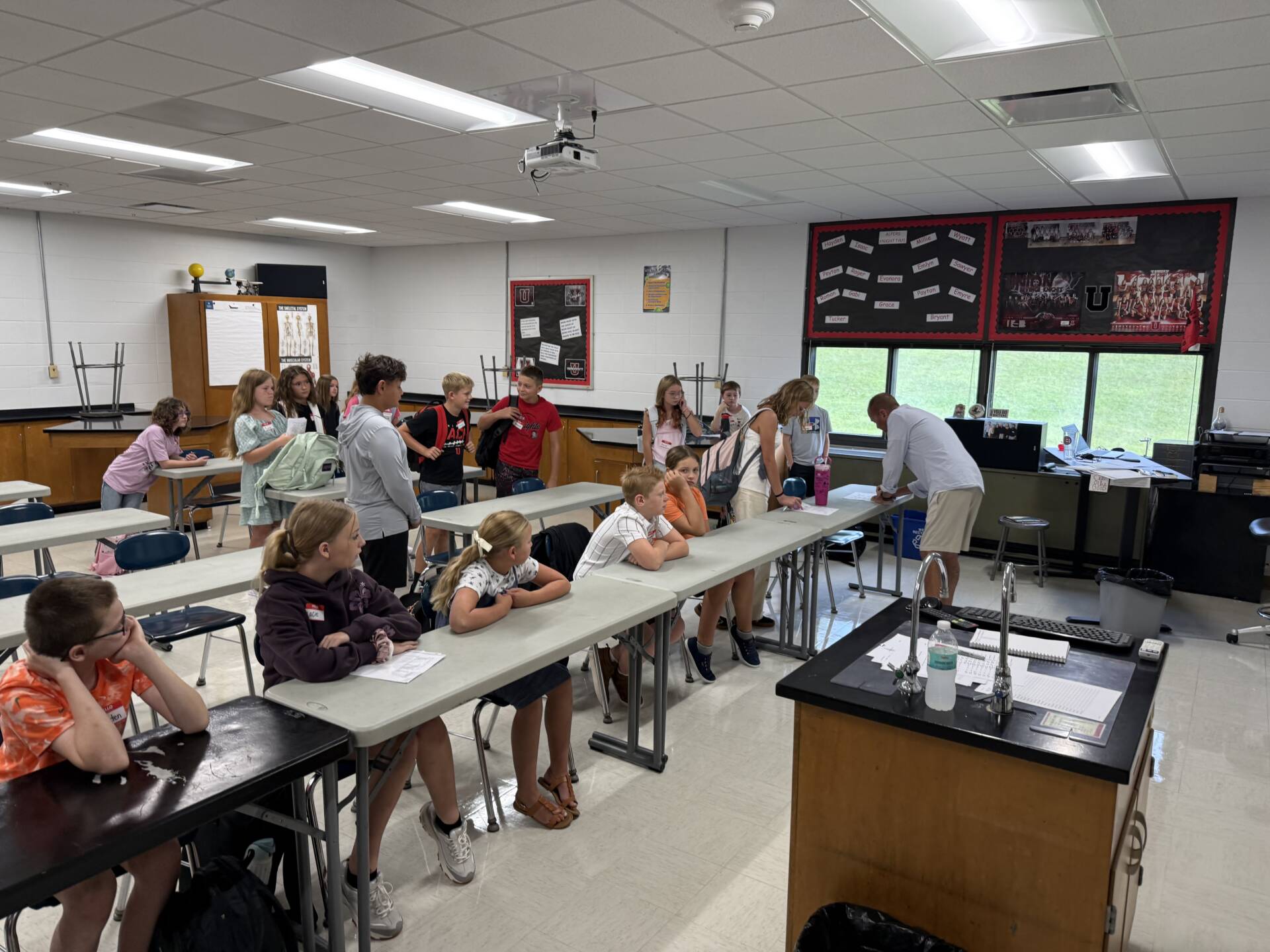 Students gather in a science classroom, talking and working together at lab tables during a school activity.