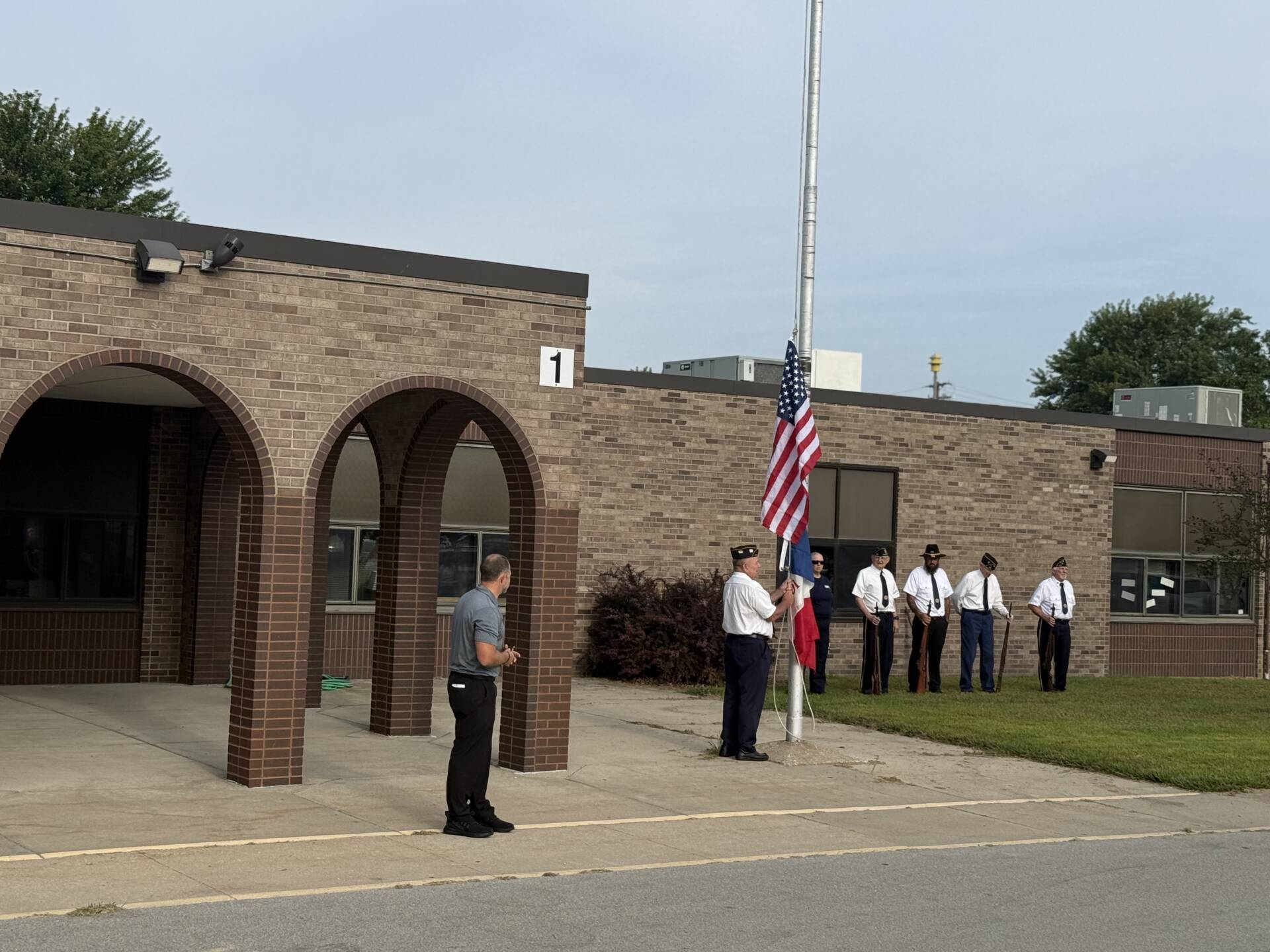 Veterans gather beside a school flagpole as a member raises the American flag during an outdoor ceremony.