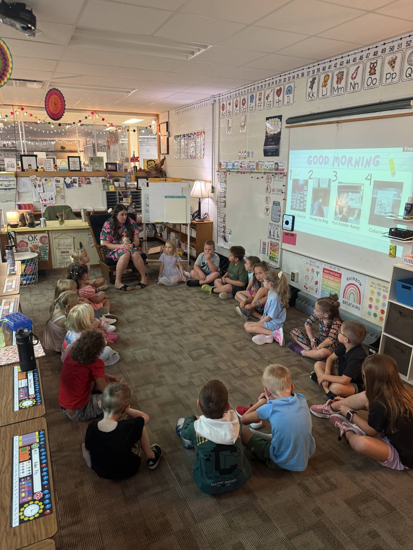 Elementary students sit in a large circle around their teacher during a morning classroom gathering.