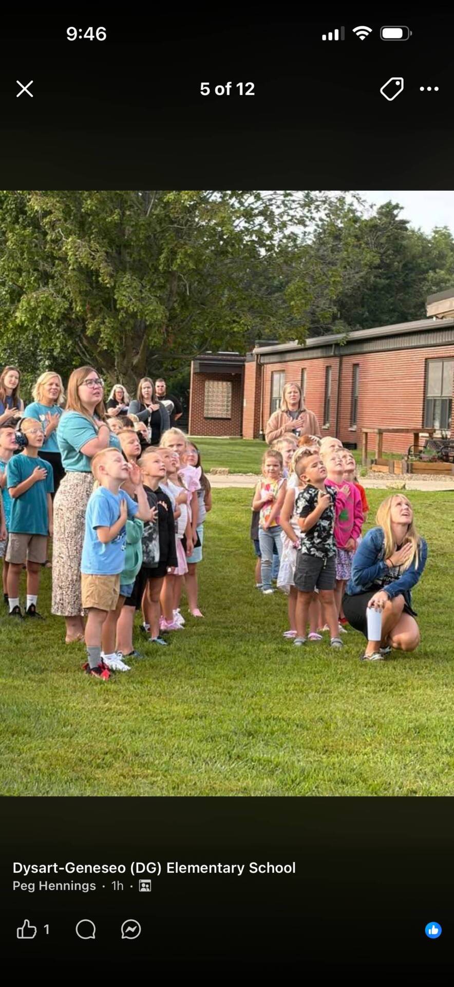 Students and staff stand outdoors with hands over their hearts during a school flag ceremony.