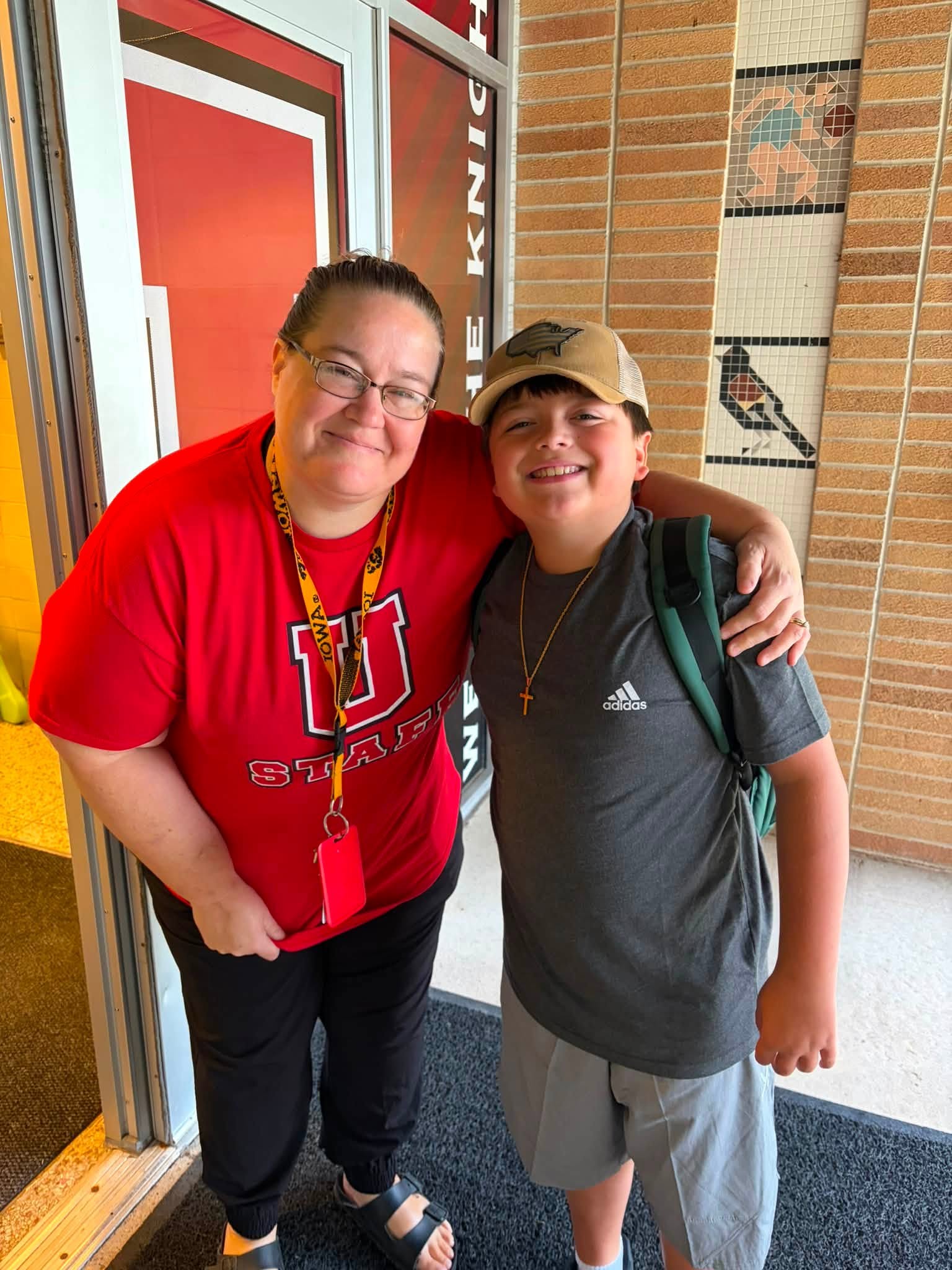 Smiling staff member puts an arm around a student wearing a backpack as they pose together in a school hallway.