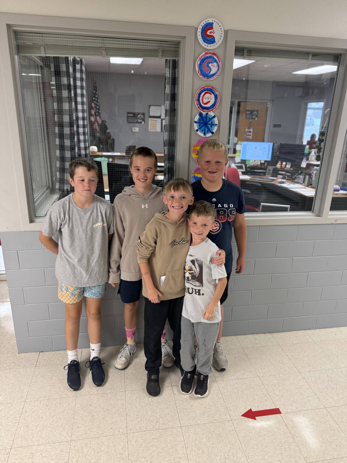 Five smiling students pose together in a school hallway beneath a display of colorful circular artwork.