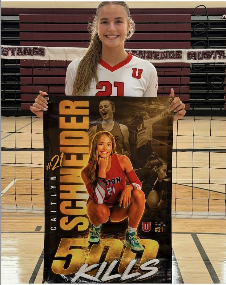 Smiling volleyball player in jersey 21 holds a personalized senior banner featuring action photos of her.