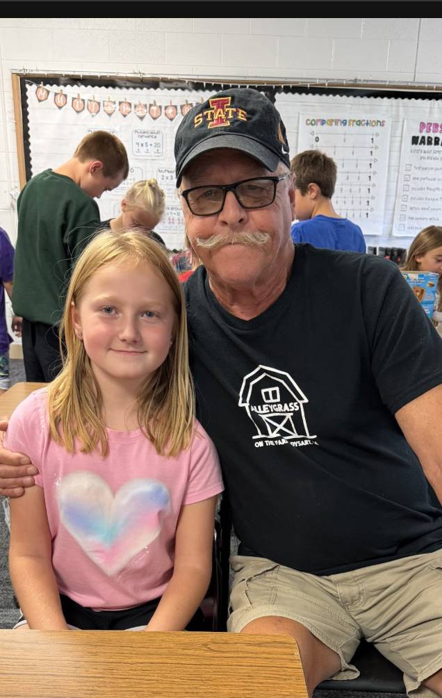 A student and older adult sit side by side and smile for a photo during a classroom activity.