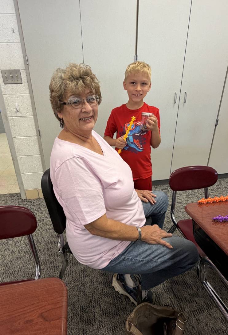 An older adult and a smiling student pose together in a classroom while holding colorful building pieces.