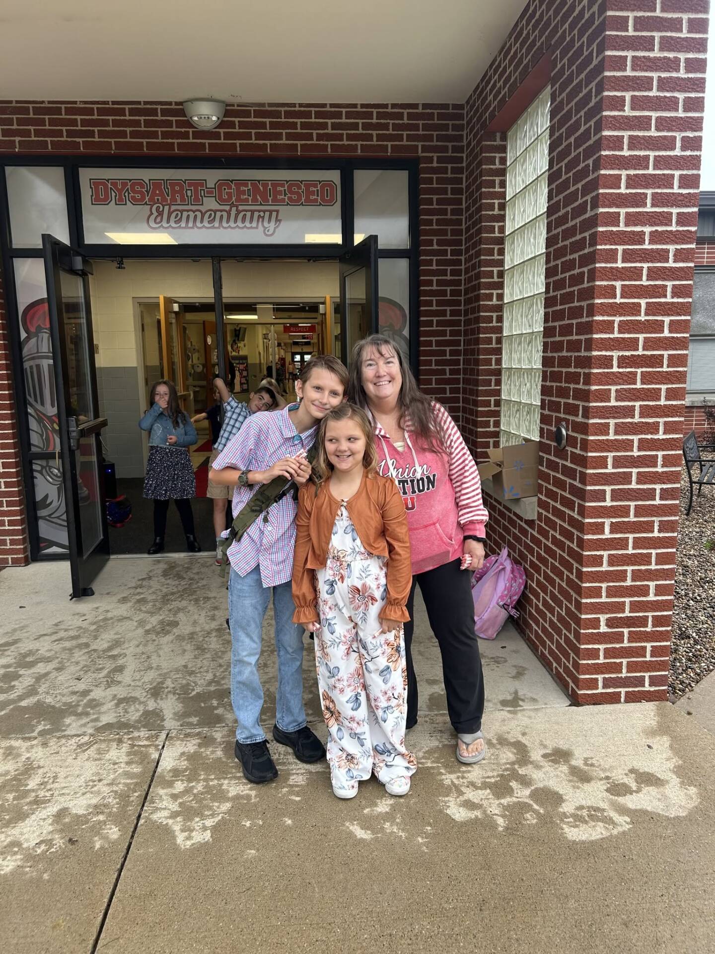 An adult and two children smile together outside the entrance to Dysart-Geneseo Elementary Schoo