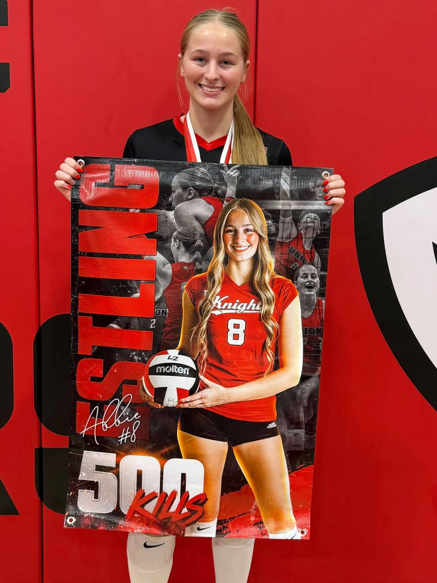 A smiling volleyball player wearing a medal holds a personalized banner celebrating 500 career kills.
