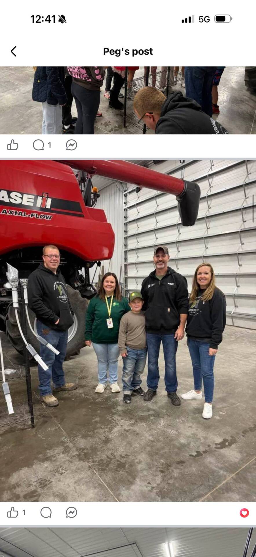 Four adults and a child pose together beside a large red combine during an agricultural learning experience.