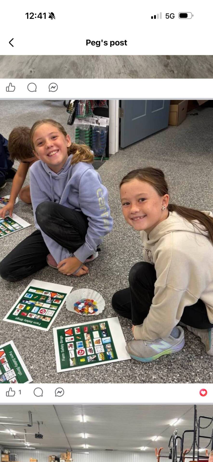 Two smiling students kneel beside Farm Safety Bingo cards and colorful game markers spread across the classroom floor.