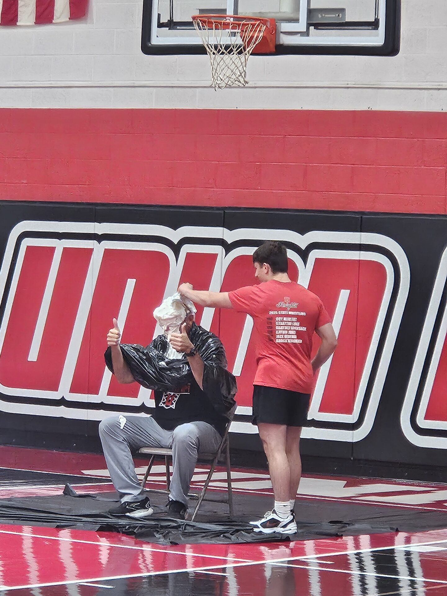 Student covers a staff member’s head with whipped cream during a gym event.
