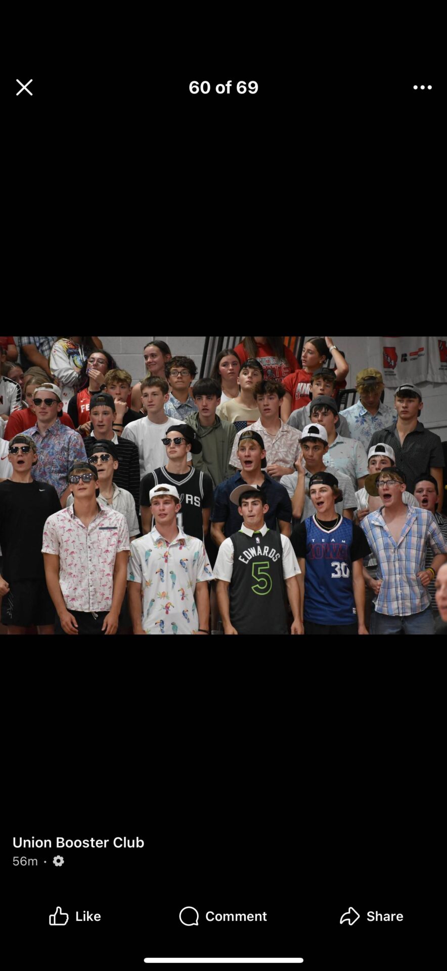 Group of students dressed in themed outfits and sunglasses cheering in the bleachers.