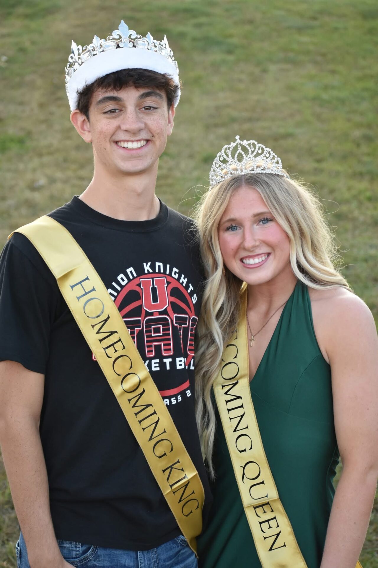 Homecoming King and Queen wearing crowns and gold sashes, smiling together.