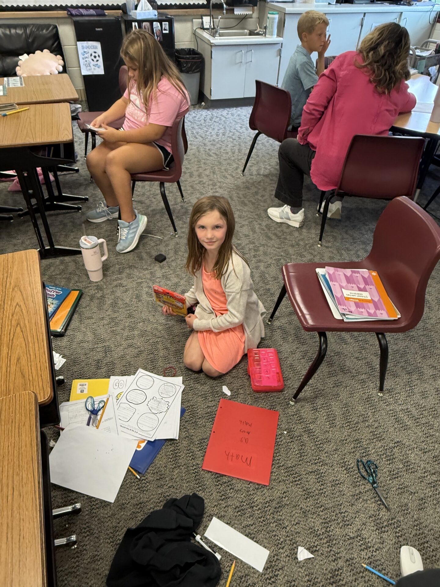 Student sitting on the floor with school supplies spread out around her.