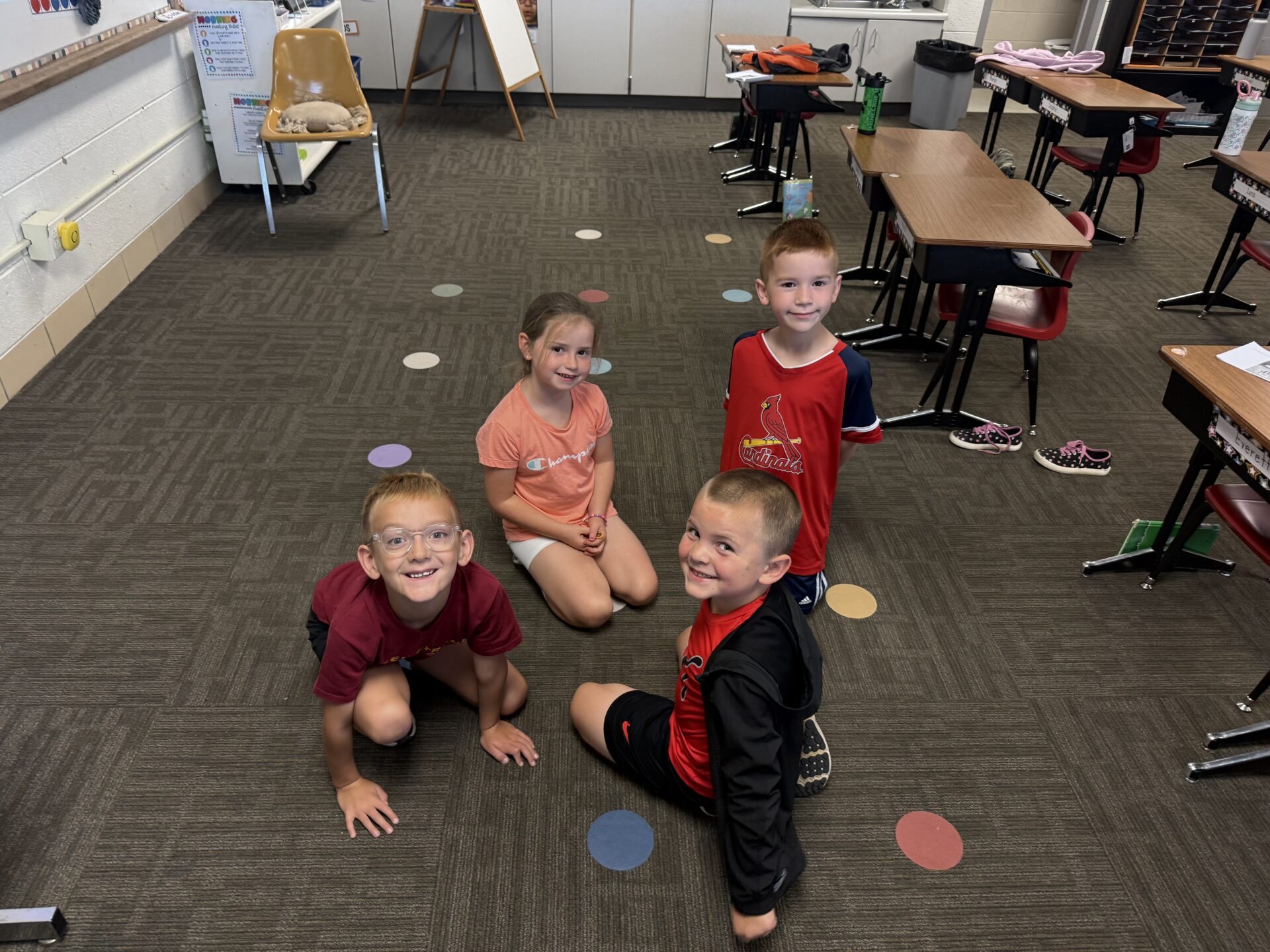 Four smiling elementary students sit on the classroom floor together for a group activity.