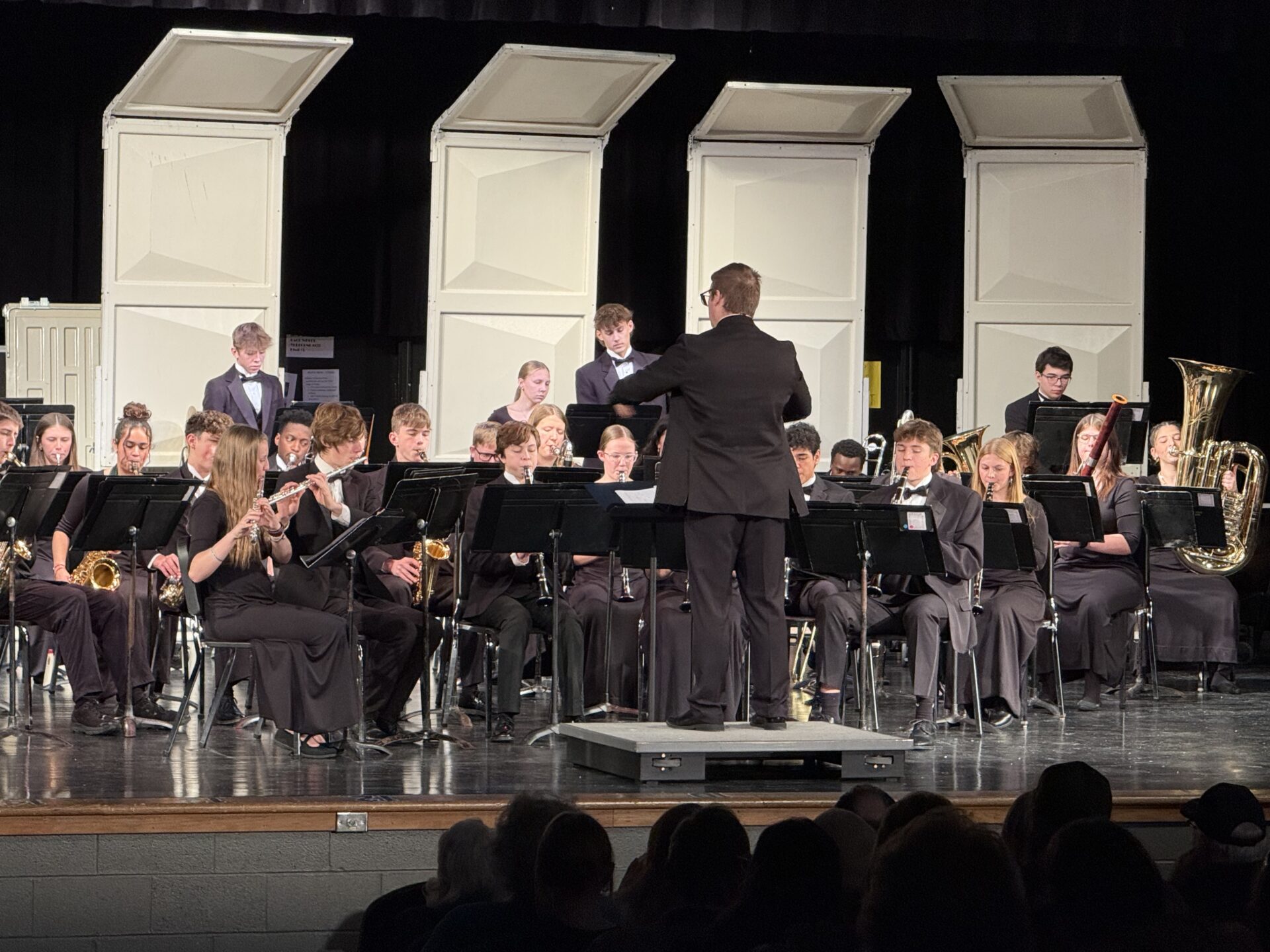 A close-up view of the high school concert band. The conductor faces the musicians, leading the performance.
