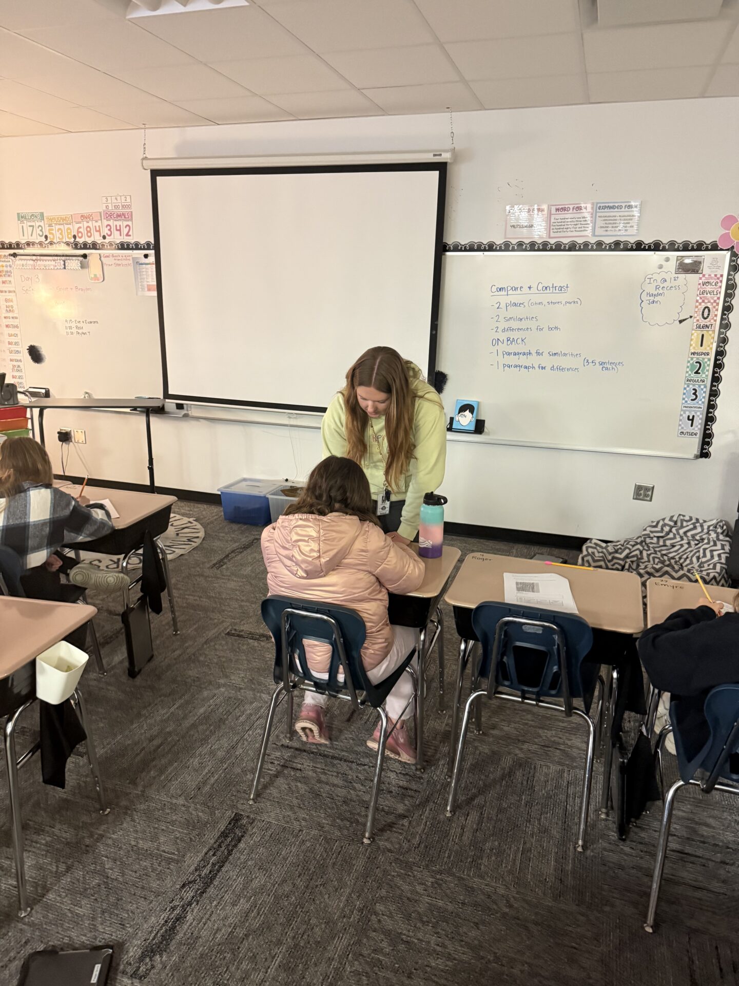 Teacher helps a student at their desk in a classroom.