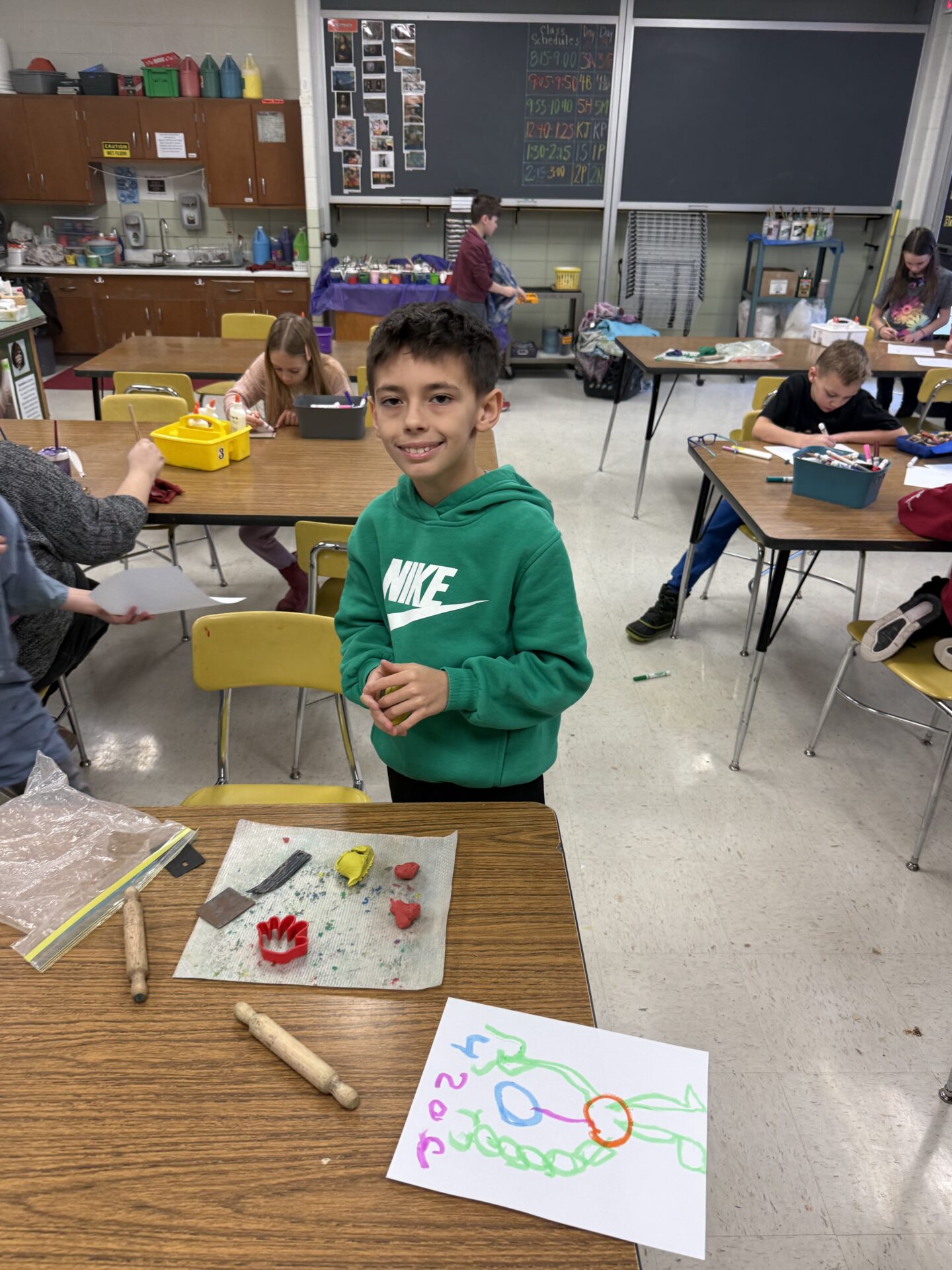 Student in green hoodie works with red and yellow clay in art class.