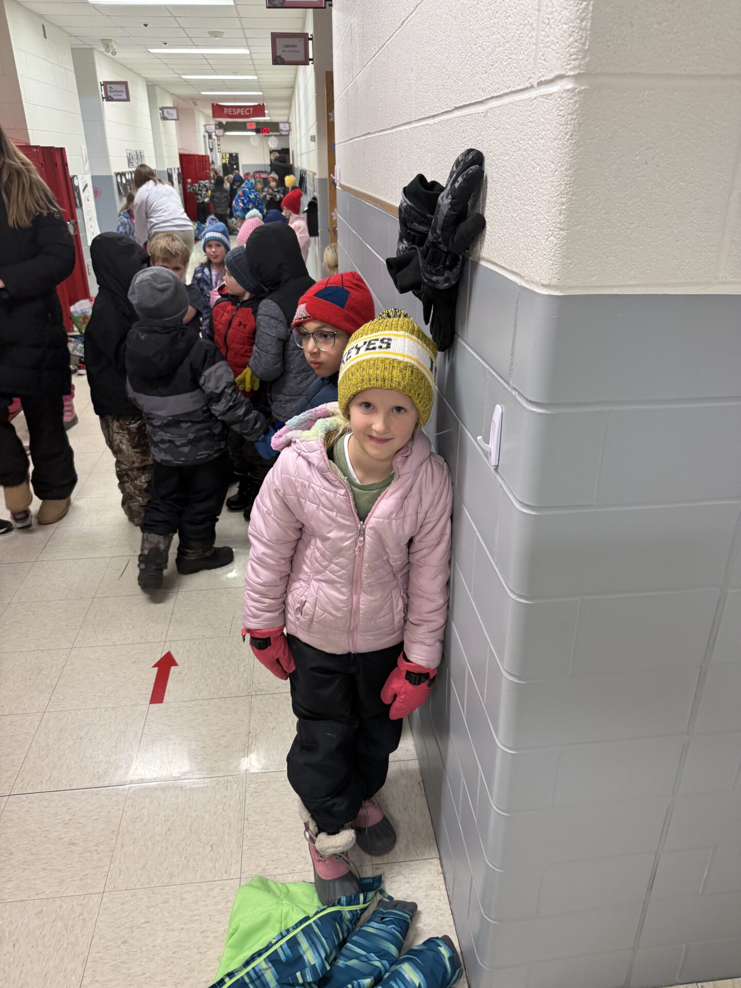 Young students in winter gear line up in a school hallway.
