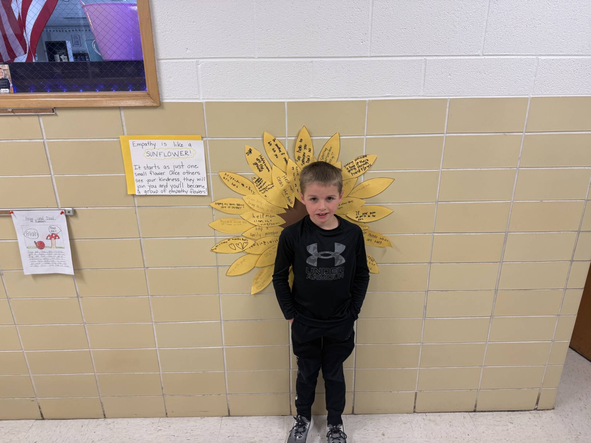 Student stands in front of a sunflower display labeled with empathy messages on a school hallway wall.