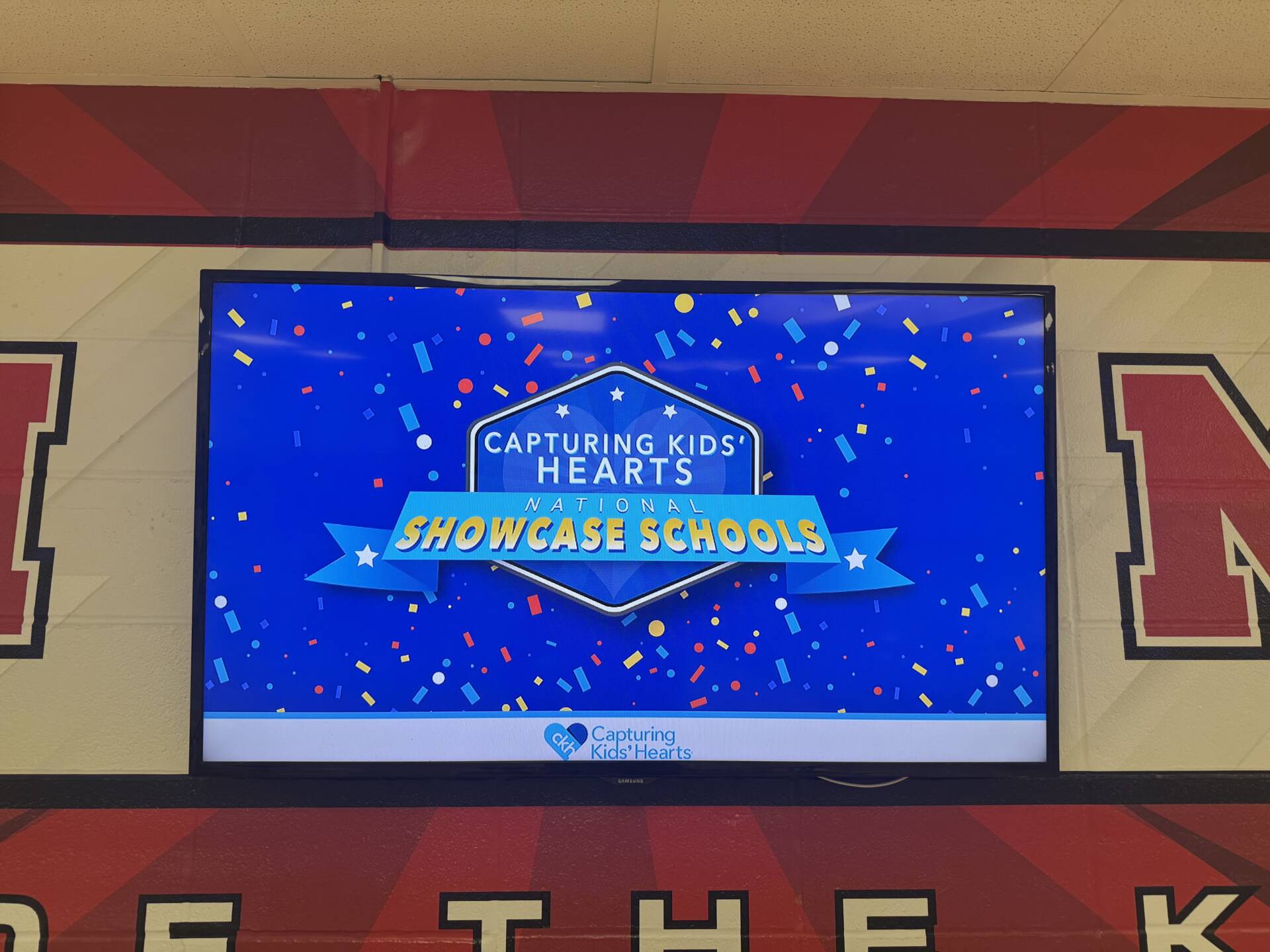 Display screen shows “Capturing Kids’ Hearts National Showcase Schools” with colorful confetti on a blue background.