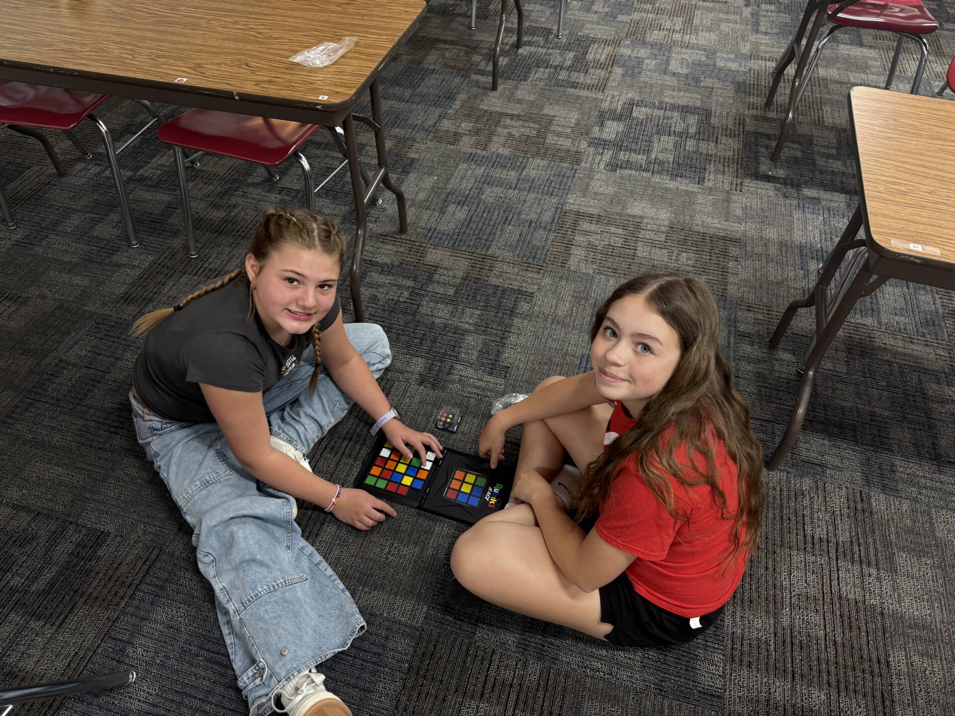 Two students sit on the floor using color grid boards, working together on a hands-on learning activity.