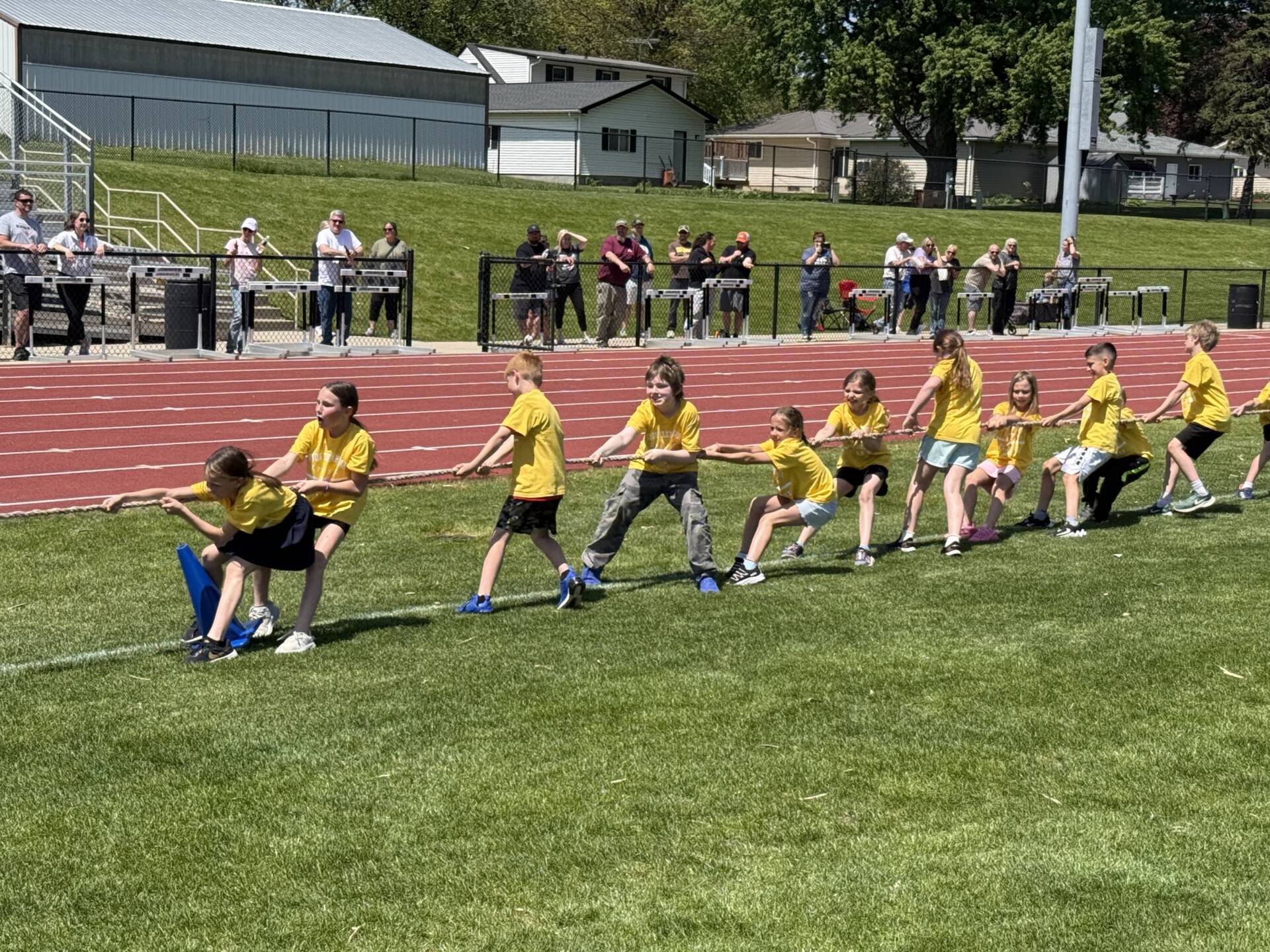 Children in yellow shirts compete in a tug-of-war game during an outdoor school field day event.