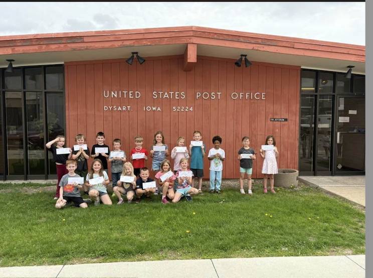 Group of elementary students pose outside a United States Post Office, each holding a letter or card.