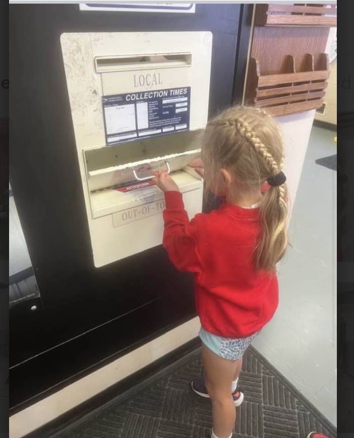 Young child with braided hair places an item into a mail slot.