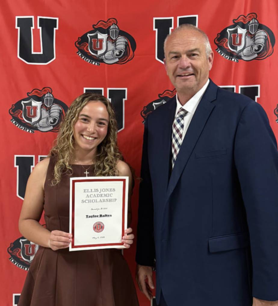 Student holds Ellis Jones Academic Scholarship certificate while posing with a school administrator against a red backdrop.