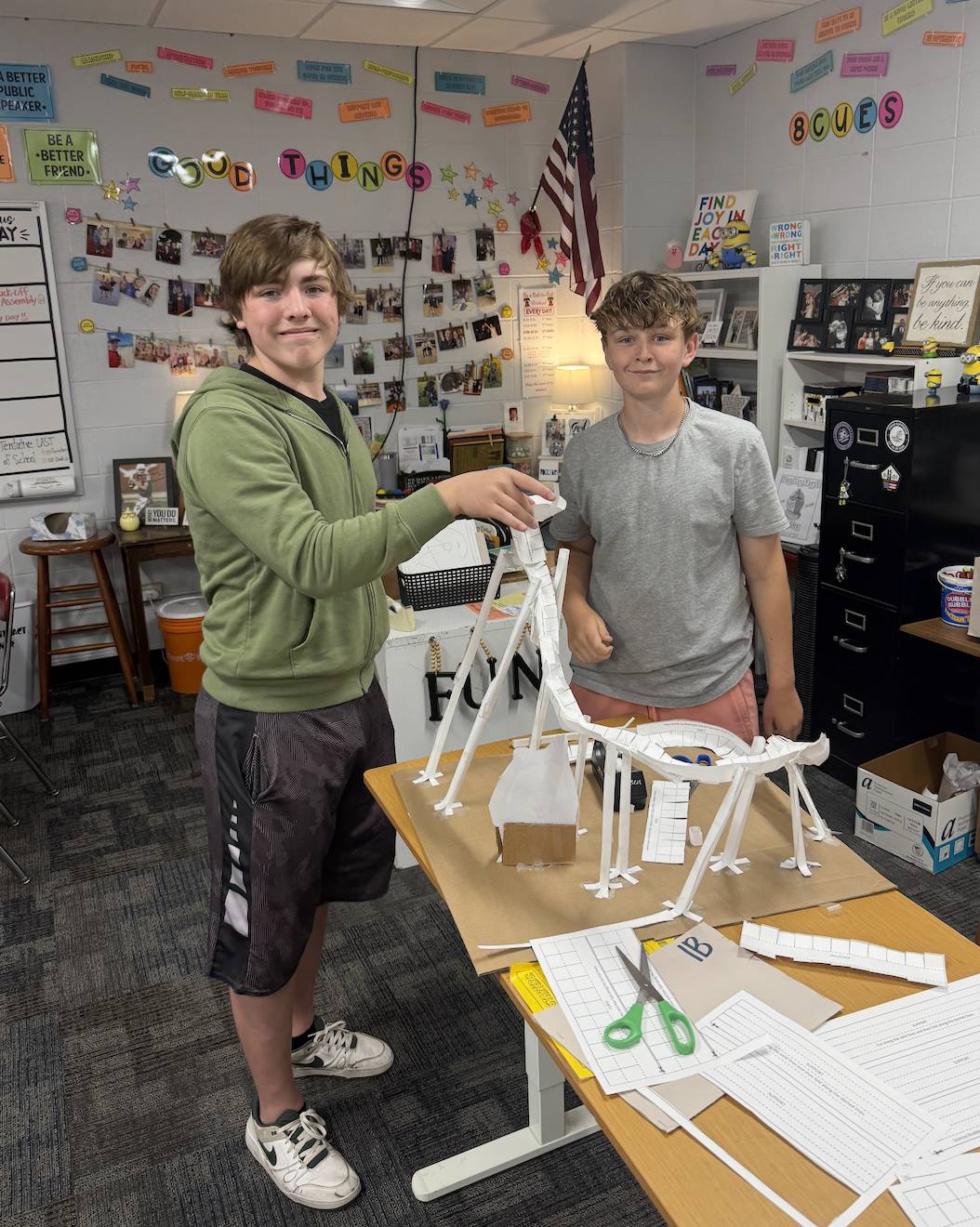 Two students stand beside a paper roller coaster model they designed and built in a classroom.