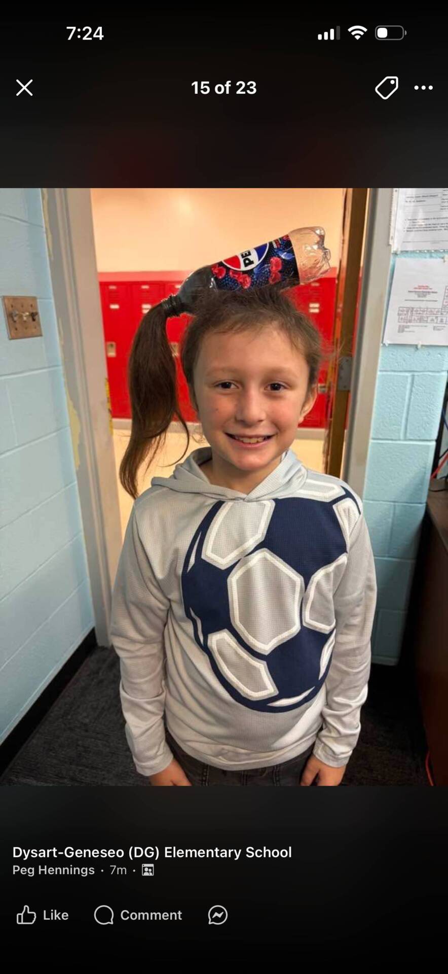 Smiling student wearing a soccer-themed hoodie and a playful decorated ponytail stands in a school doorway.