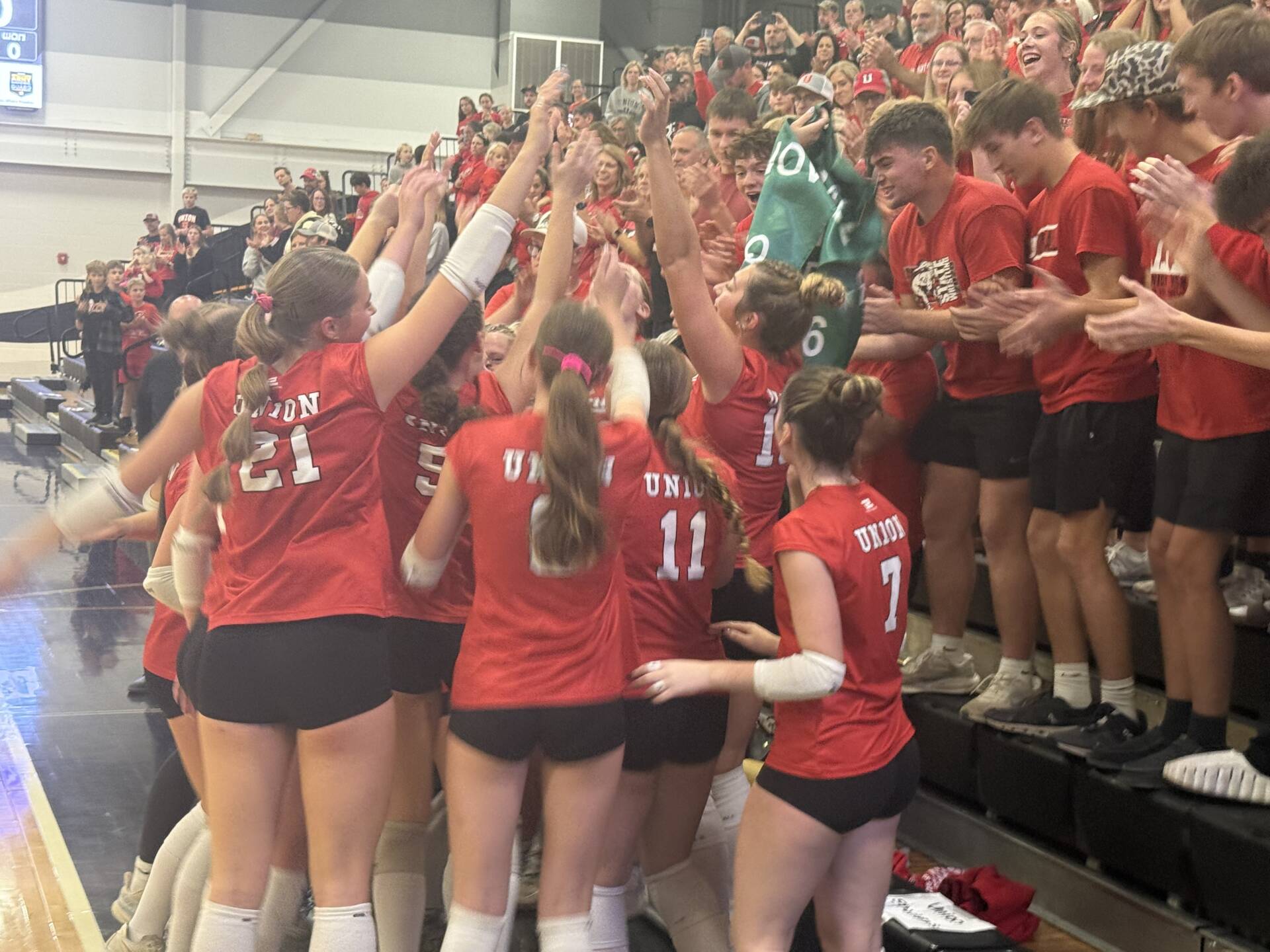 Union volleyball players in red uniforms celebrate with cheering fans, exchanging high-fives in a packed gymnasium.