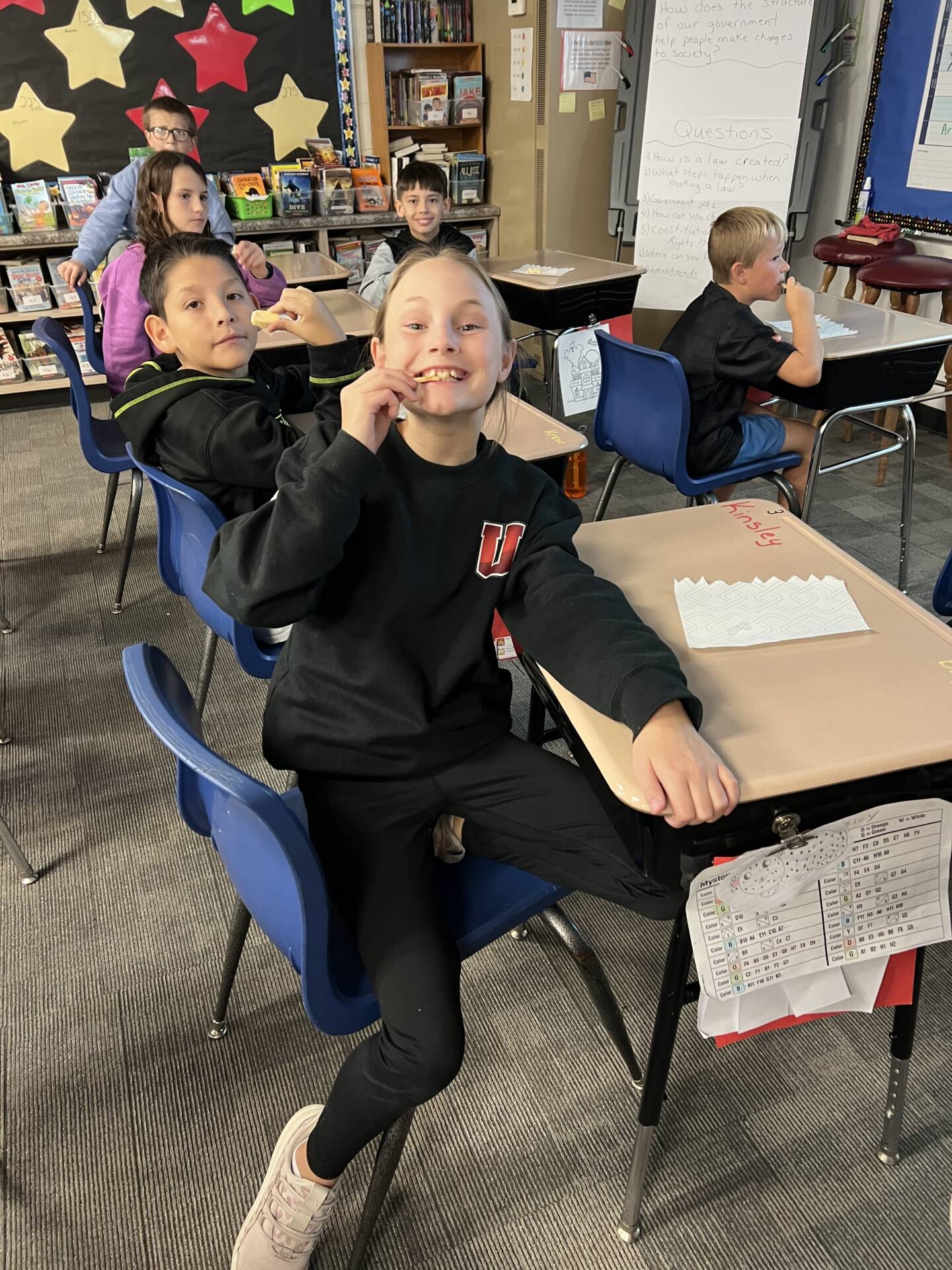 A smiling student in a black Union sweatshirt samples a snack while classmates participate in a classroom tasting activity.
